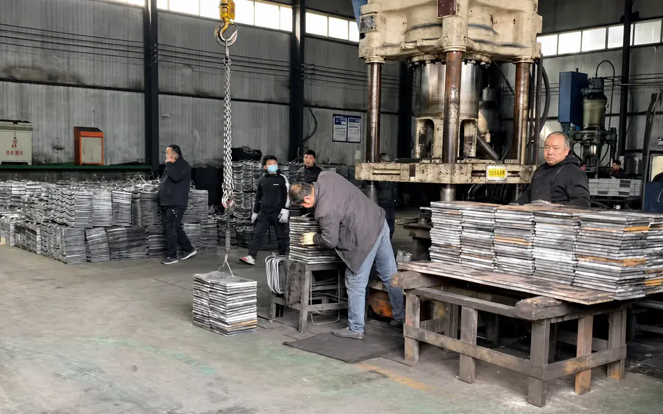 Workers handling stacked steel plates beside forming equipment in the Xianhong Mining workshop